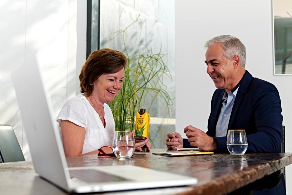 older woman and man with an aloe vera drink smiling sitting at a table
